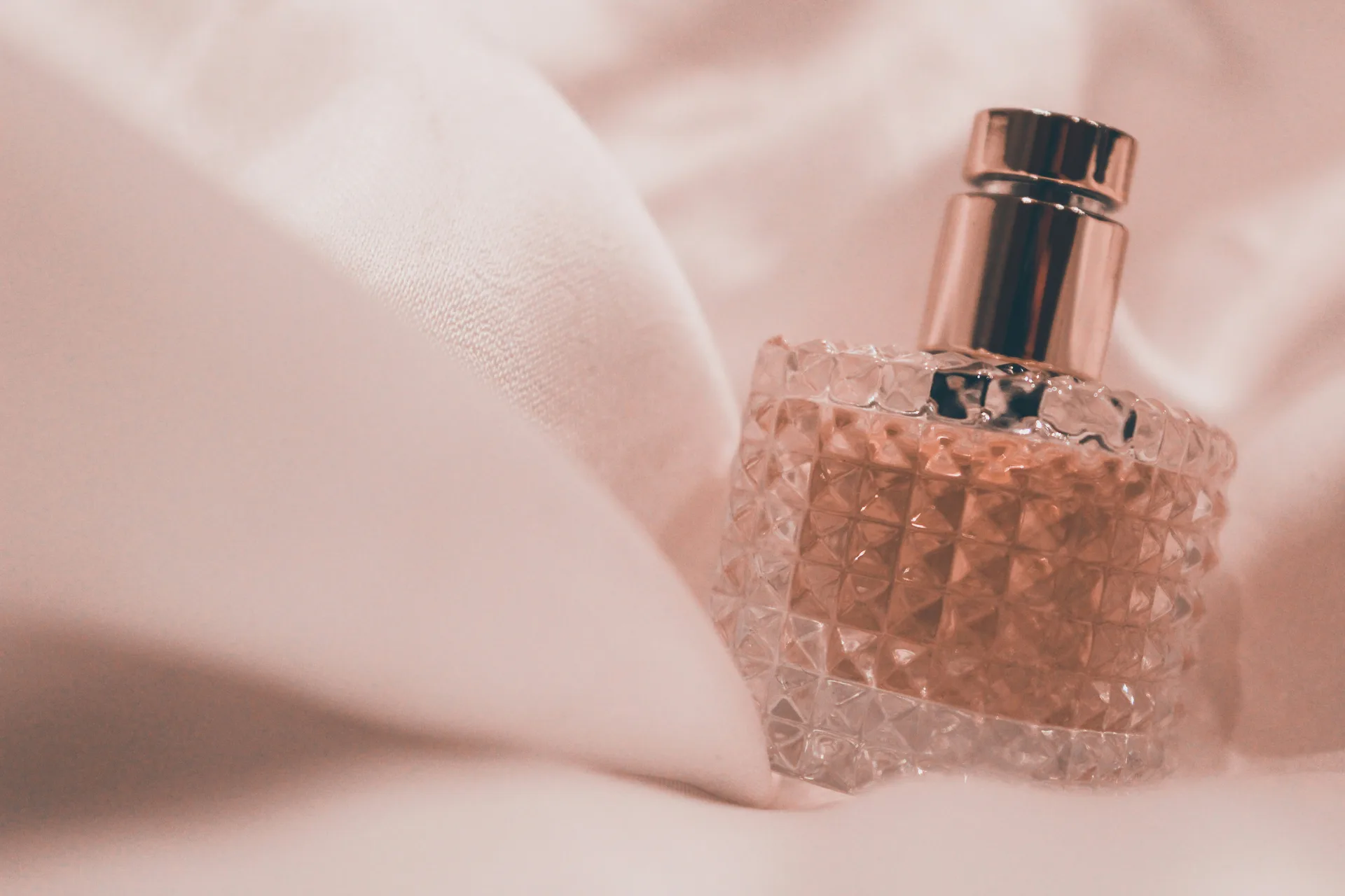 A faceted perfume bottle resting against soft pink satin